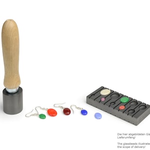 May include: A set of five colourful glass beads for jewellery making. The beads are displayed in a black mould with a wooden handle press. The beads are green, red, blue, white, and pink.