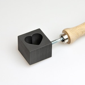 May include: A black graphite heart-shaped mold with a wooden handle. The mold is attached to the handle with a metal screw.