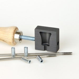 Könnte beinhalten: Ein Satz Metallwerkzeuge zur Herstellung von Schmuck. Das Set enthält eine Presse mit Holzgriff, eine Graphitform und mehrere Metallstangen mit Gewindeenden.