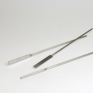 May include: Three stainless steel mixing spatulas with rectangular blades and long, thin handles are arranged diagonally against a white background. The spatulas are designed for laboratory or kitchen use.