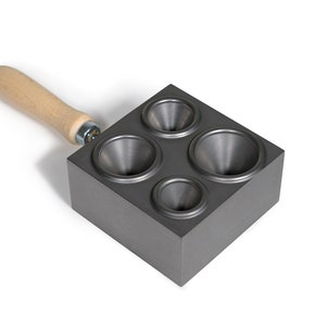 May include: A gray metal mold with four funnel-shaped cavities and a wooden handle. The mold is used for casting metal.