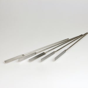 May include: Five silver metal rods with flat, rectangular ends. The rods are arranged in a fan shape.