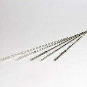 May include: A set of six silver metal knitting needles of varying lengths.