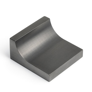 Op de afbeelding: Een donkergrijze metalen kastknop met een gebogen, afgeronde bovenkant en een vierkante basis.