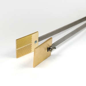 May include: A pair of silver tongs with two brass plates attached. One plate has a textured surface and the other is smooth.