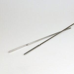 May include: Two silver chopsticks, crossed over each other, on a white background.