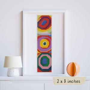 May include: A colorful cross-stitch pattern with three concentric circles in shades of red, yellow, green, blue, and purple. The pattern is framed and measures 2 by 8 inches.