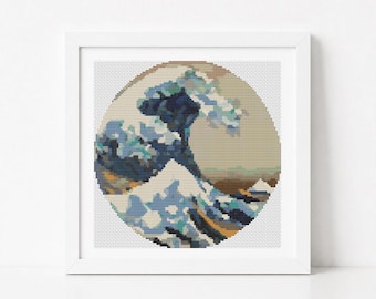 May include: A square white frame containing a circular cross-stitch embroidery piece. The design depicts a stylized ocean wave in shades of dark blue, light blue, and white, set against a beige background, mimicking a classic Japanese woodblock print.
