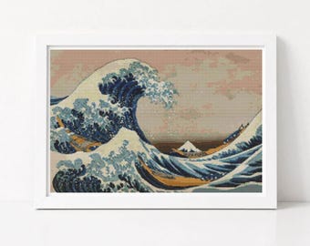 May include: A framed cross-stitch embroidery depicting a large, cresting blue wave with white foam, inspired by The Great Wave off Kanagawa. The scene features a distant white mountain peak against a muted, light-coloured sky in a rectangular frame.
