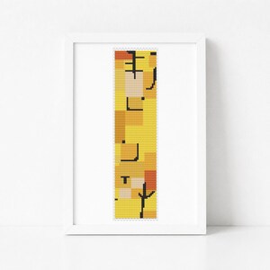 May include: A framed cross-stitch pattern featuring a vertical rectangular design with a pixelated abstract motif in shades of yellow, orange, and white, accented by thin black lines and geometric shapes, presented in a simple white frame.