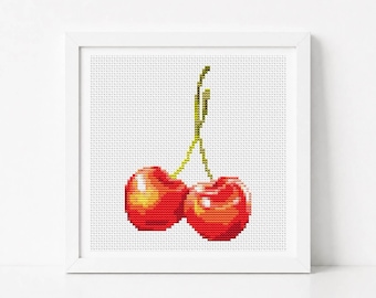 May include: A square white frame containing a cross-stitch embroidery of two bright red cherries with green stems. The cherries feature yellow and orange highlights to create a sense of depth and light reflection against the white fabric background.