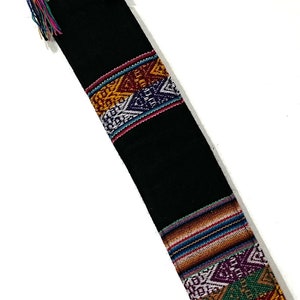 May include: Black fabric bag with colourful geometric patterns and tassels. The bag is woven with a traditional design.