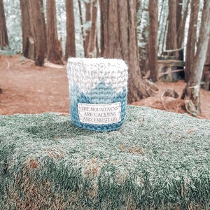 May include: A blue and white crocheted cup cozy with the text "The mountains are calling and I must go."