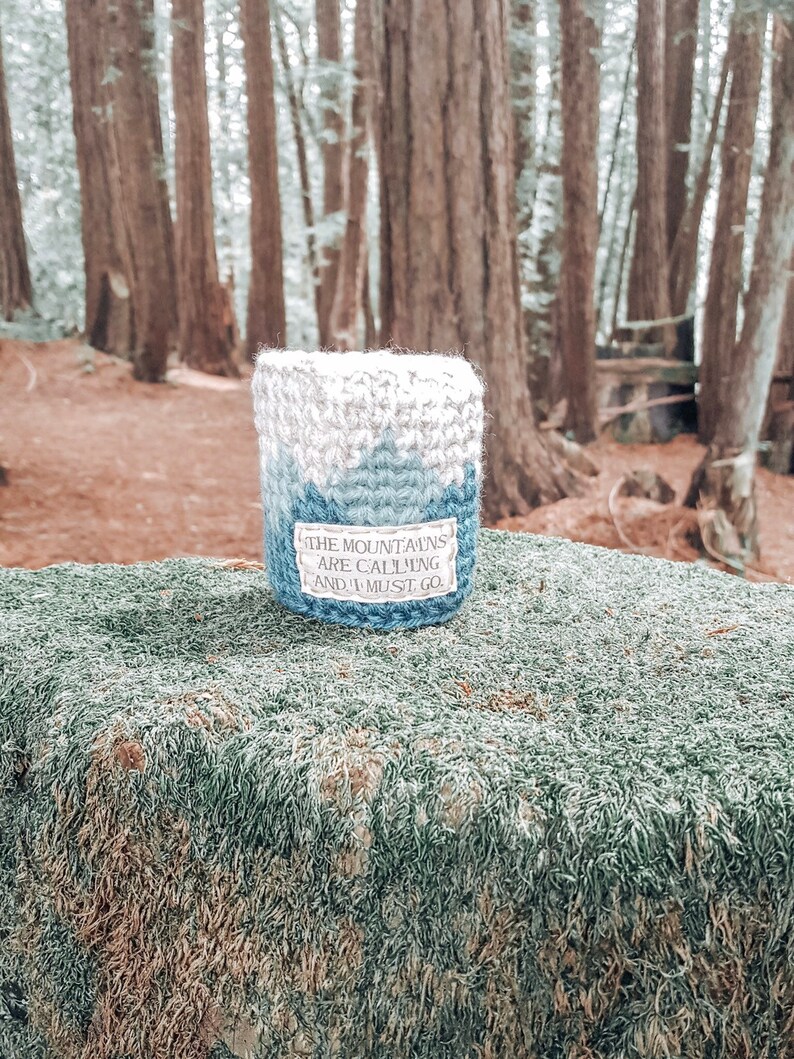 May include: A blue and white crocheted cup cozy with the text "The mountains are calling and I must go."