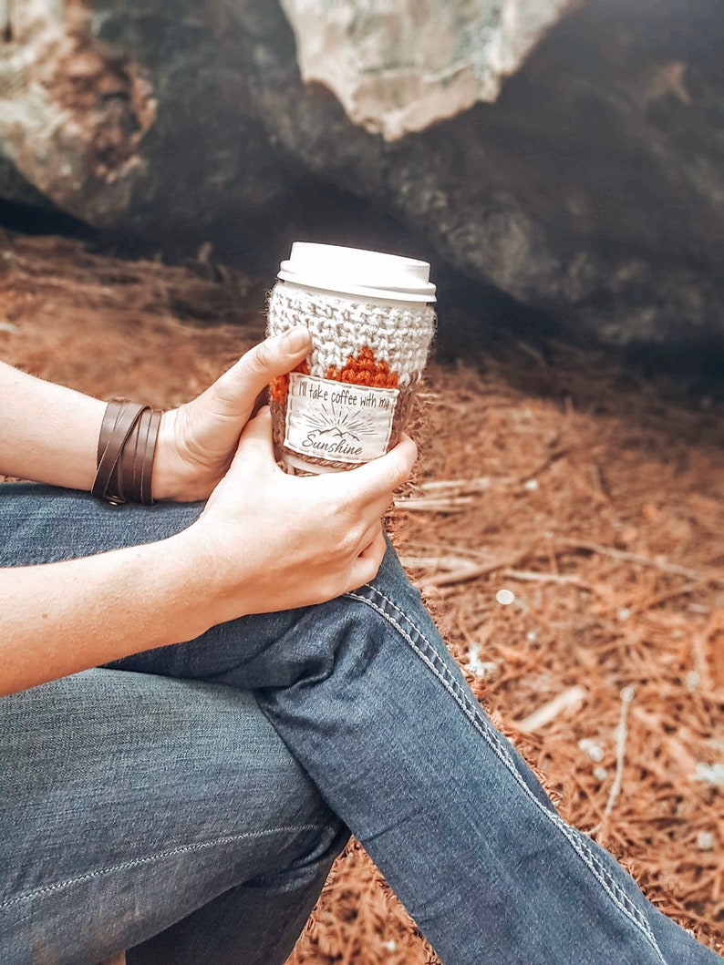May include: A white crocheted coffee cup cozy with a brown label that reads "I'll take coffee with you Sunshine".