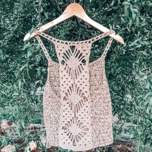 May include: A crocheted tank top with a delicate openwork design at the back. The top is made with a beige yarn with brown and white flecks.
