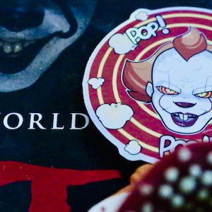 Op de afbeelding: Een ronde sticker in rood en wit met een cartoonafbeelding van Pennywise de clown uit de film "IT". De sticker heeft het woord "POP!" meerdere keren erop geschreven.