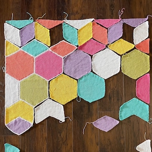 May include: A colourful crochet blanket made of various hexagons and triangles in shades of pink, yellow, green, and white.