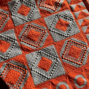 May include: A crocheted blanket with a patchwork design featuring orange and gray squares. The blanket is made with a variety of stitches, including bobbles and circles.