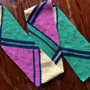 May include: A crocheted scarf with a geometric pattern in shades of pink, green, yellow, and blue.
