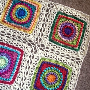 May include: A white crochet blanket with colorful square motifs. Each square features a circular design with multiple layers of different colored yarn. The blanket is made with a delicate openwork pattern.