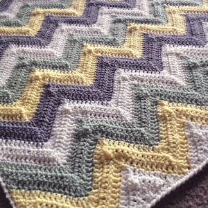 May include: A crocheted chevron baby blanket in white, gray, and yellow.