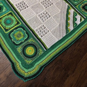 May include: A crocheted blanket with a white center and a green border. The border is made up of multiple rows of different shades of green.