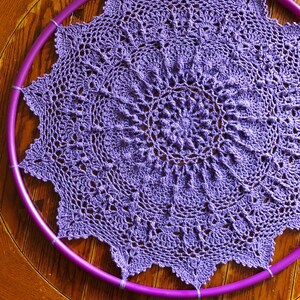 Op de afbeelding: Een paarse gehaakte doily is gespannen over een paarse plastic hoepel.