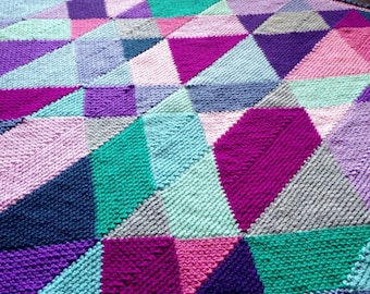 May include: A colorful knitted blanket with a geometric pattern of triangles in shades of pink, purple, blue, and green.