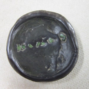 May include: A round, black, ceramic dish with a raised rim. The dish is decorated with small, green glass pieces.