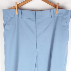 May include: Light blue trousers hanging on a wooden hanger. The pants have a classic design with a straight leg and a button and zipper closure. The trousers are made of a smooth, solid-colored fabric.