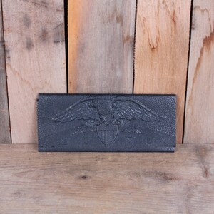 May include: A black leather wallet with an embossed eagle and shield design. The wallet has the words "U.S. MAIL" embossed on the front.