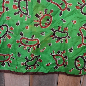May include: A green silk scarf with a brown border. The scarf features a repeating pattern of brown and orange circles with various shapes and designs inside.