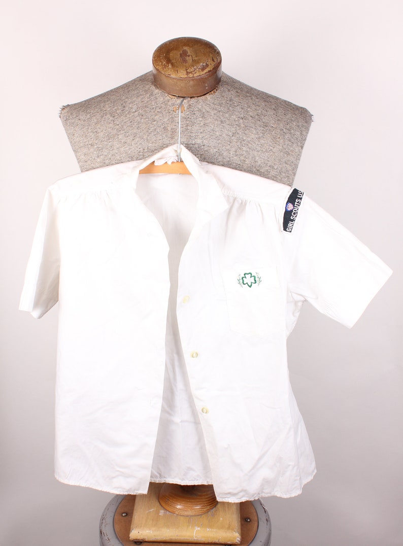 Puede incluir: Camisa blanca de manga corta con botones, con un logotipo bordado verde de Girl Scout en el pecho izquierdo y un parche de Girl Scouts USA en la manga derecha.