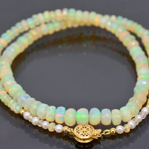 May include: A double strand necklace made of white opal beads with a gold clasp. The necklace is accented with small white pearl beads.