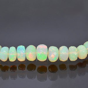 May include: A strand of white opal beads with a faceted, barrel shape. The beads have a slight iridescent sheen.