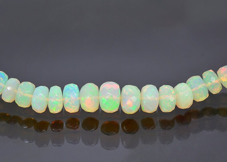 May include: A strand of white opal beads with a faceted, barrel shape. The beads have a slight iridescent sheen.