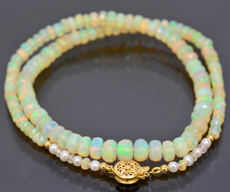 May include: A double strand necklace made of white opal beads with a gold clasp. The necklace is accented with small white pearl beads.