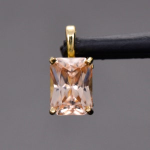 May include: A gold pendant featuring a light pink, rectangular-shaped gemstone with a faceted cut.
