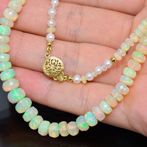 May include: A delicate necklace made with white opal beads and a gold clasp. The necklace is displayed on a hand.