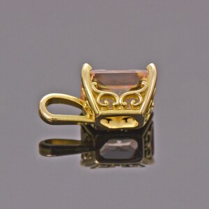 May include: A gold pendant with a light brown gemstone set in a decorative frame. The pendant has a loop for attaching to a chain.