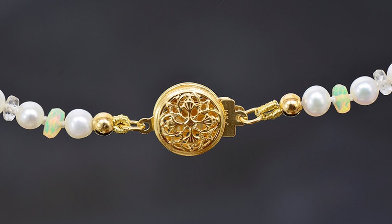 May include: A gold necklace with a decorative clasp and white pearls and opals.