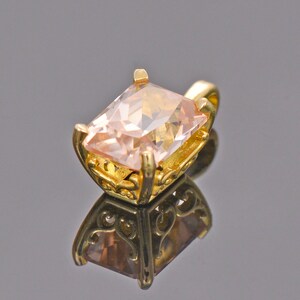 May include: A gold pendant with a large, light pink, square-shaped gemstone set in a delicate, ornate frame.