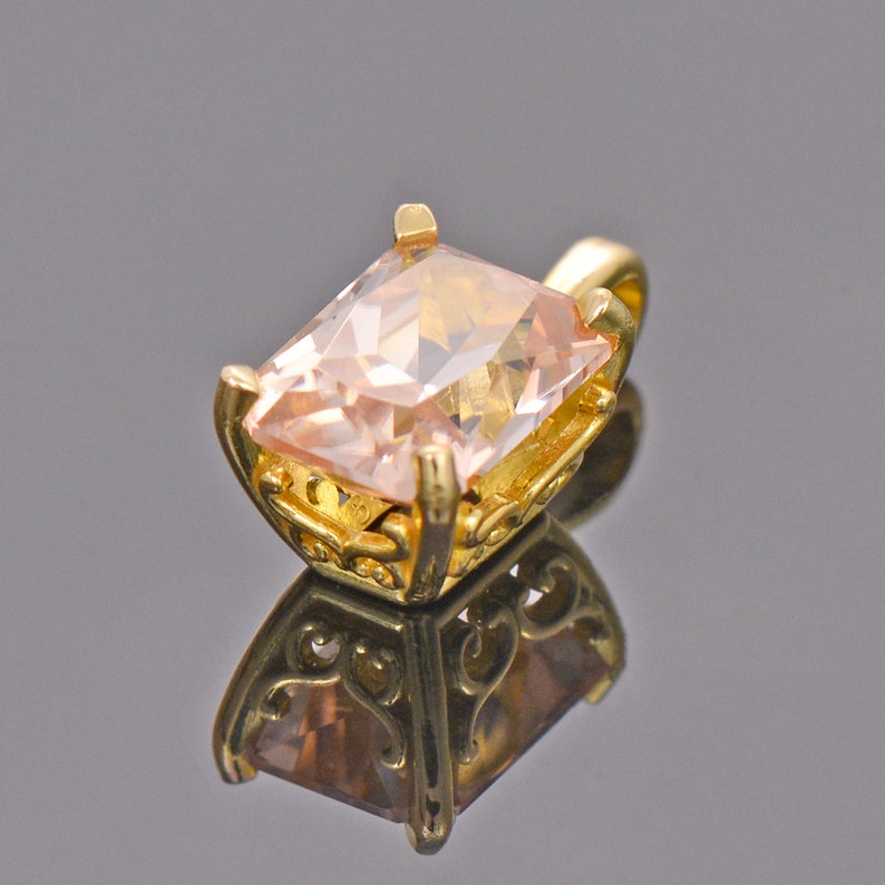 May include: A gold pendant with a large, light pink, square-shaped gemstone set in a delicate, ornate frame.