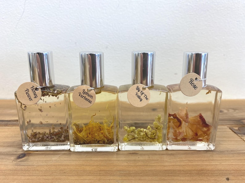May include: Four small glass bottles with silver caps and brown labels. The labels have different floral scents: Honey Flower, Lemon Verbena, Lily of the Valley, and Rose.
