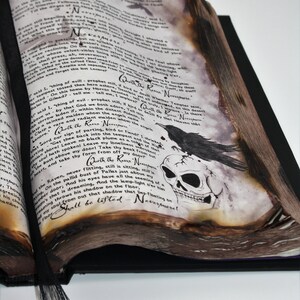 May include: A vintage book with a dark, gothic aesthetic. The pages are open to reveal a skull with a raven perched on top. The text on the page reads "Quoth the Raven Nevermore".