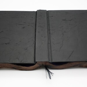 May include: A black book with a textured cover is open and lying flat. The book has a black ribbon bookmark.