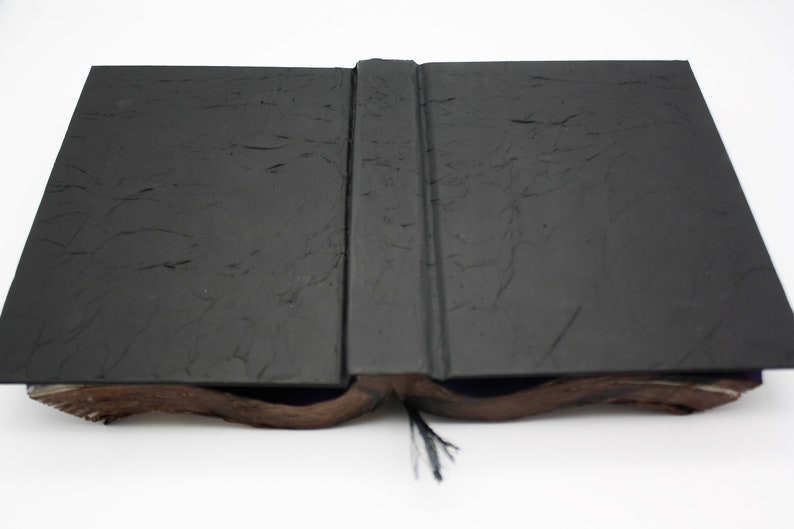 May include: A black book with a textured cover is open and lying flat. The book has a black ribbon bookmark.