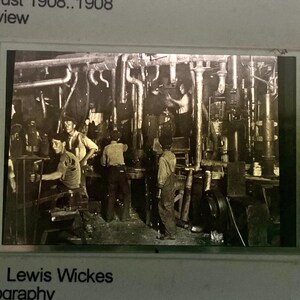 May include: A square photographic slide featuring a black and white image of workers in a factory. The frame includes printed text: Hine, L-PHOTO, Indiana Glass Works. 9:00 PM, August 1908, 1908, full view, and Hine, Lewis Wickes photography, U of Virginia FAIC.