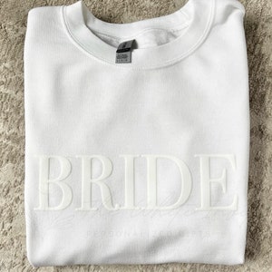 May include: White sweatshirt with the word "BRIDE" printed in raised white letters.